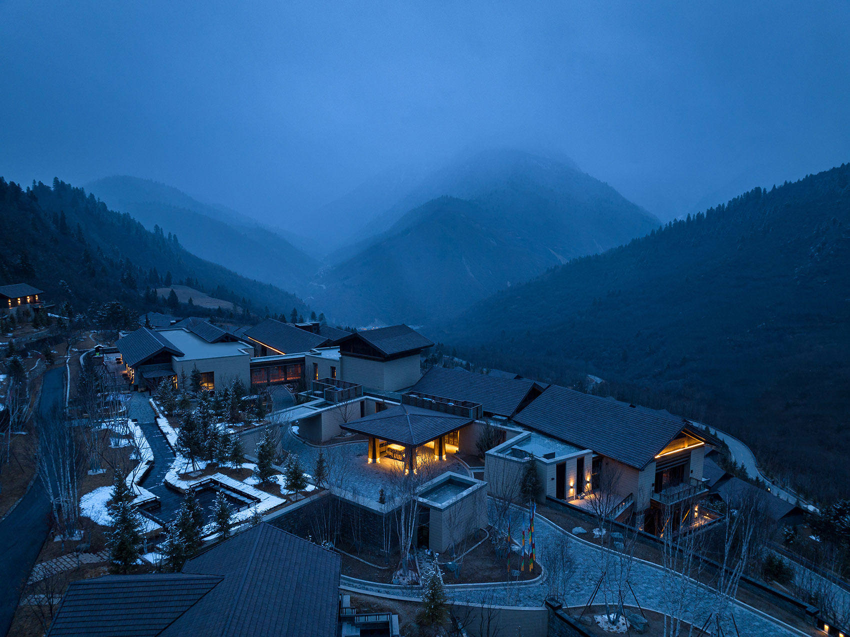 日赛谷公区夜景，暖光从藏式碉楼体量的建筑中透出，木构与格栅在夜色中呈现仪式感